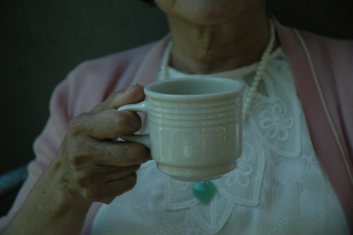 Mains âgées tenant une tasse vert d'eau
